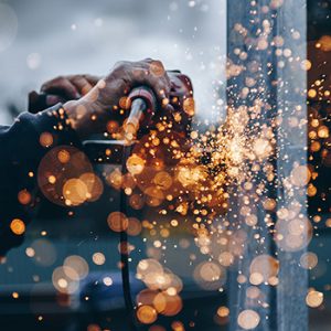 construction worker's hands using a power tool on metal that is creating sparks everywhere