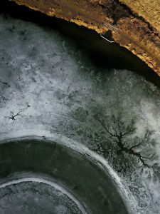 aerial view of a frozen lake and the shore with shack and deck